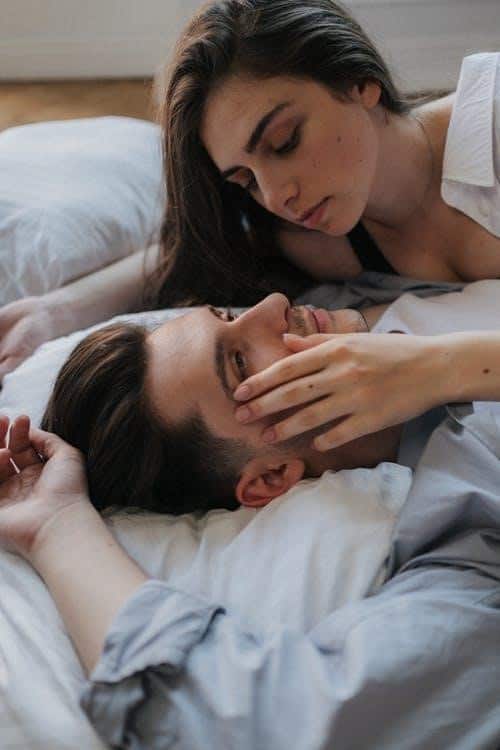 A Man Lying in Bed and Staring Off in Space While a Woman Leans Over and Caresses His Face